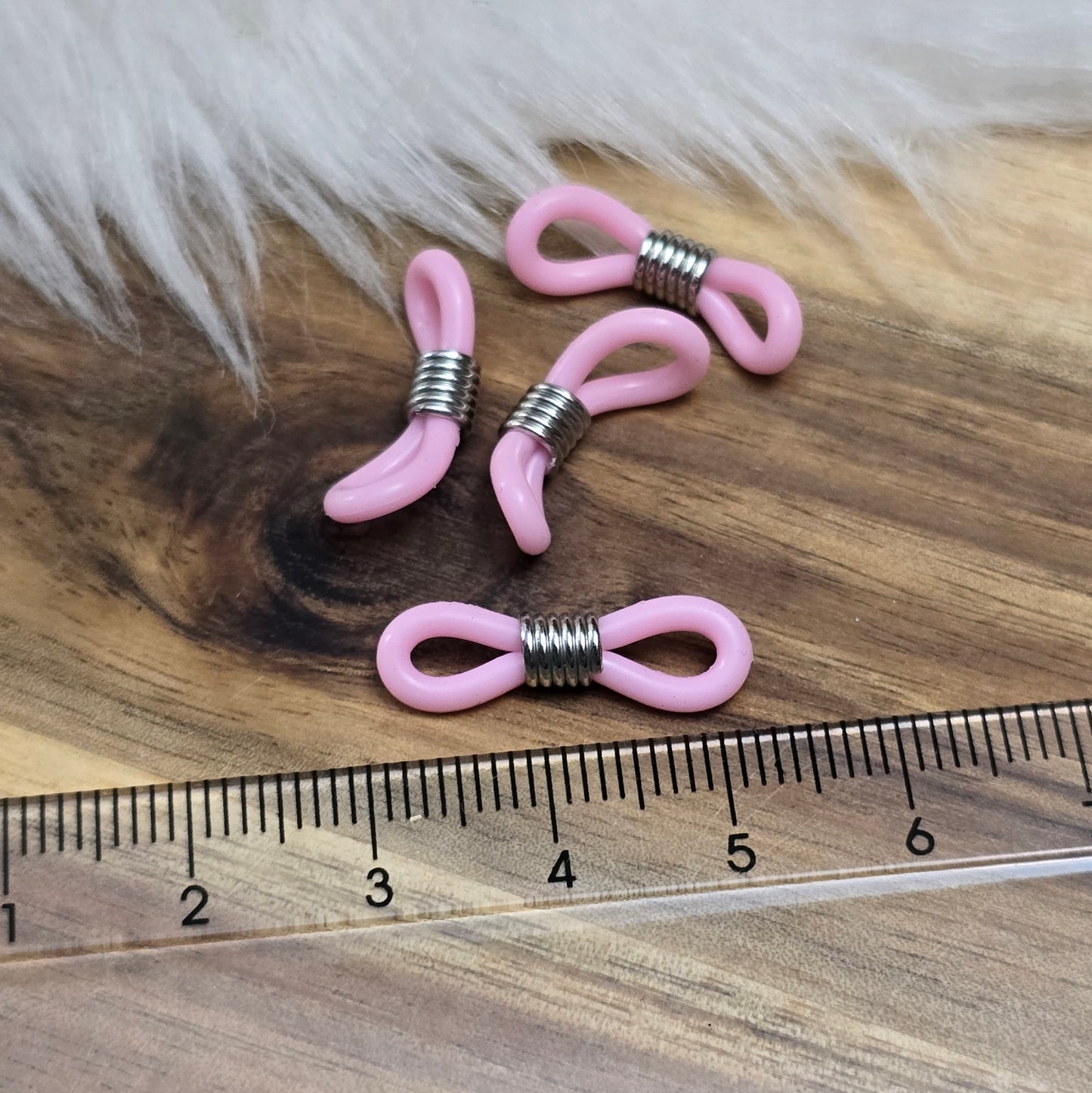 Das Bild zeigt eine Auswahl an Silikonschlaufen für Brillenketten und Maskenhalter in drei Farben: Mint, Rosa und Schwarz. Jede Schlaufe hat eine flexible, weiche Textur und ist so gestaltet, dass sie einfach auf den Bügel der Brille geschoben werden kann. An einem Ende der Schlaufe befindet sich ein kleiner Metallring, der fest angebracht ist, um ein Abrutschen zu verhindern. Die anderen Enden der Schlaufen sind offen, sodass sie mit einem Karabiner oder Biegering leicht an einer Kette befestigt werden kön