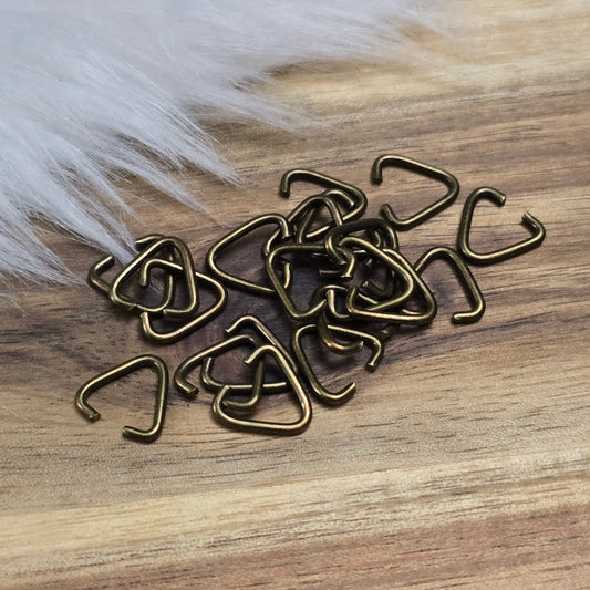 Das Bild zeigt ein Set mit 40 offenen Triangel-Ösen aus antik bronzefarbener Eisenlegierung, die eine Höhe von 9 mm haben. Die Ösen sind in Form eines gleichseitigen Dreiecks gestaltet, wobei eine Seite offen ist, um das Einfügen von Schmuckkomponenten zu erleichtern. Die matte, antik bronzefarbene Oberfläche verleiht den Ösen einen charmanten Vintage-Look, der ideal für verschiedene Schmuckherstellungsprojekte ist. Das Set ist übersichtlich angeordnet und hebt die Vielseitigkeit dieser Ösen hervor, die per