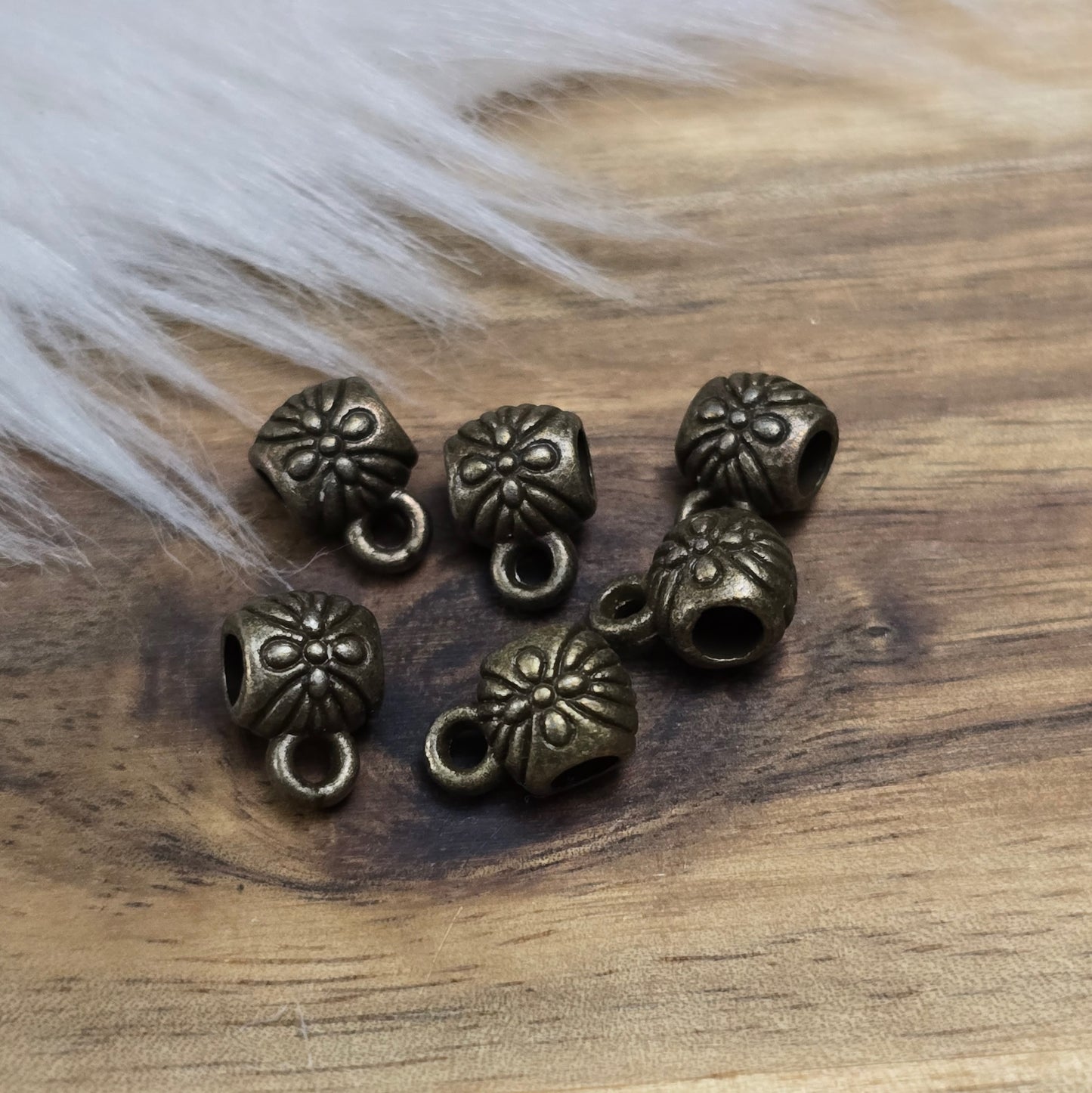 Das Bild zeigt ein Set von 6 antik bronzefarbenen Metallperlen mit Anhängerösen, die einen Durchmesser von etwa 6 mm haben. Jede Perle ist mit einer praktischen Anhängeröse ausgestattet, die es ermöglicht, sie leicht an Ketten oder Armbändern zu befestigen. Die Metallperlen besitzen ein großzügiges Fädelloch, das das Einfädeln von Schnüren oder Drähten erleichtert. Ihr antik bronzefarbiges Finish verleiht ihnen eine elegante und zeitlose Ästhetik, die sich ideal für die Herstellung individueller Schmuckstüc