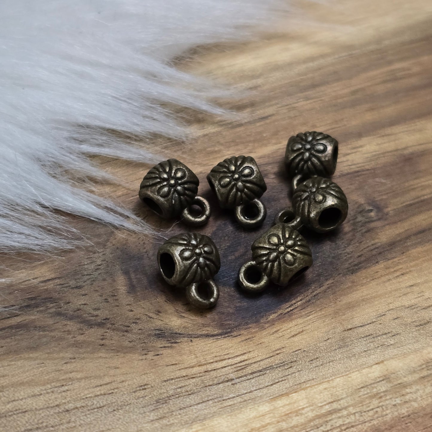 Das Bild zeigt ein Set von 6 antik bronzefarbenen Metallperlen mit Anhängerösen, die einen Durchmesser von etwa 6 mm haben. Jede Perle ist mit einer praktischen Anhängeröse ausgestattet, die es ermöglicht, sie leicht an Ketten oder Armbändern zu befestigen. Die Metallperlen besitzen ein großzügiges Fädelloch, das das Einfädeln von Schnüren oder Drähten erleichtert. Ihr antik bronzefarbiges Finish verleiht ihnen eine elegante und zeitlose Ästhetik, die sich ideal für die Herstellung individueller Schmuckstüc