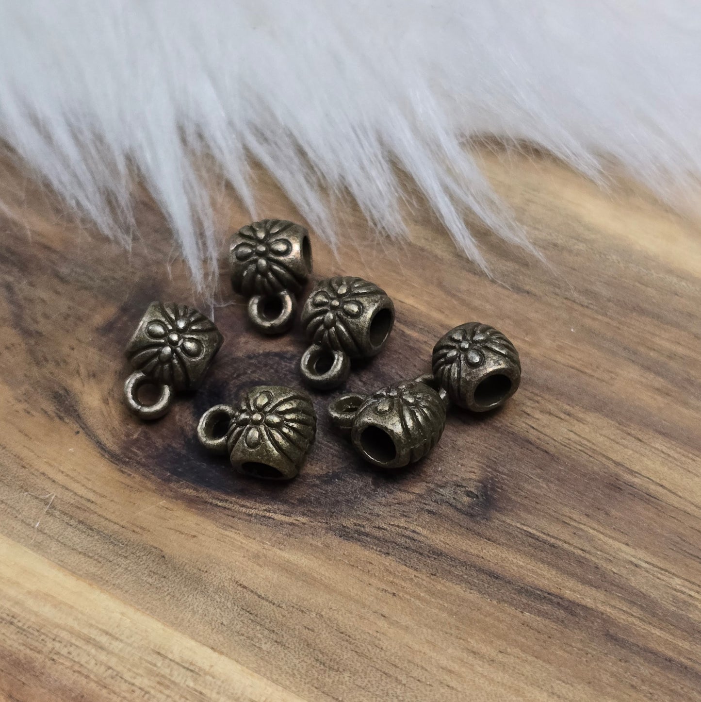 Das Bild zeigt ein Set von 6 antik bronzefarbenen Metallperlen mit Anhängerösen, die einen Durchmesser von etwa 6 mm haben. Jede Perle ist mit einer praktischen Anhängeröse ausgestattet, die es ermöglicht, sie leicht an Ketten oder Armbändern zu befestigen. Die Metallperlen besitzen ein großzügiges Fädelloch, das das Einfädeln von Schnüren oder Drähten erleichtert. Ihr antik bronzefarbiges Finish verleiht ihnen eine elegante und zeitlose Ästhetik, die sich ideal für die Herstellung individueller Schmuckstüc