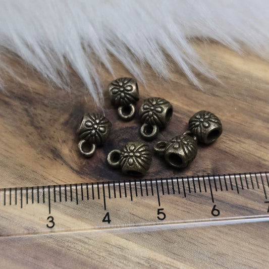 Das Bild zeigt ein Set von 6 antik bronzefarbenen Metallperlen mit Anhängerösen, die einen Durchmesser von etwa 6 mm haben. Jede Perle ist mit einer praktischen Anhängeröse ausgestattet, die es ermöglicht, sie leicht an Ketten oder Armbändern zu befestigen. Die Metallperlen besitzen ein großzügiges Fädelloch, das das Einfädeln von Schnüren oder Drähten erleichtert. Ihr antik bronzefarbiges Finish verleiht ihnen eine elegante und zeitlose Ästhetik, die sich ideal für die Herstellung individueller Schmuckstüc