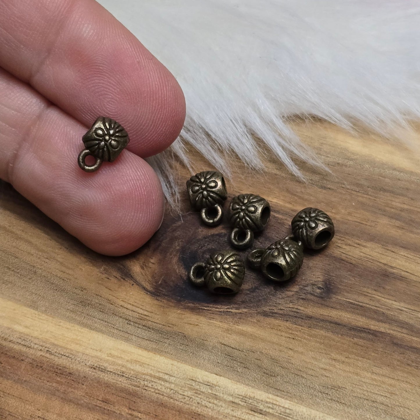 Das Bild zeigt ein Set von 6 antik bronzefarbenen Metallperlen mit Anhängerösen, die einen Durchmesser von etwa 6 mm haben. Jede Perle ist mit einer praktischen Anhängeröse ausgestattet, die es ermöglicht, sie leicht an Ketten oder Armbändern zu befestigen. Die Metallperlen besitzen ein großzügiges Fädelloch, das das Einfädeln von Schnüren oder Drähten erleichtert. Ihr antik bronzefarbiges Finish verleiht ihnen eine elegante und zeitlose Ästhetik, die sich ideal für die Herstellung individueller Schmuckstüc