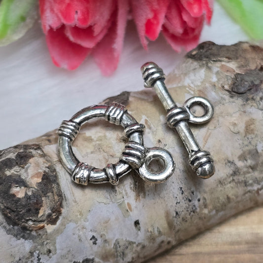 Die Abbildung zeigt zwei antik silberfarbene Knebelverschlüsse, bestehend aus einem Ring und einem Stab. Diese hochwertigen Verschlüsse bieten eine elegante Lösung für Schmuckstücke wie Armbänder und Ketten. Ihr klassisches Design verleiht jedem Projekt eine dekorative Note und sorgt gleichzeitig für eine sichere Verschlussmöglichkeit.