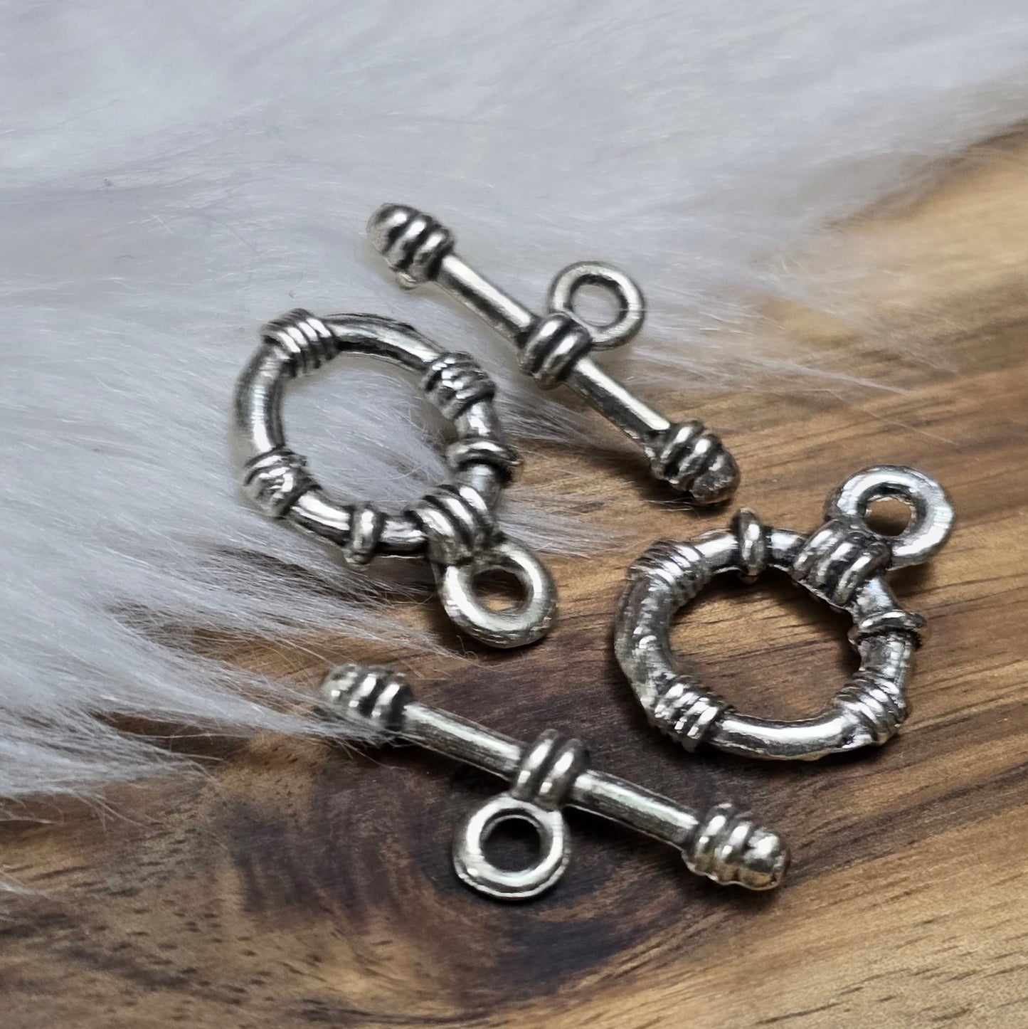 Die Abbildung zeigt zwei antik silberfarbene Knebelverschlüsse, bestehend aus einem Ring und einem Stab. Diese hochwertigen Verschlüsse bieten eine elegante Lösung für Schmuckstücke wie Armbänder und Ketten. Ihr klassisches Design verleiht jedem Projekt eine dekorative Note und sorgt gleichzeitig für eine sichere Verschlussmöglichkeit.