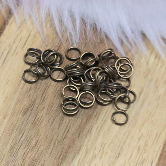 Das Bild zeigt 50 doppelte Binderinge in antikem Bronze-Finish. Die Verbindungsringe sind ein unverzichtbares Zubehör für die Schmuckherstellung. Durch ihre doppelte Wicklung bieten sie eine besonders stabile und sichere Verbindung, sodass Anhänger, Charms und Verschlüsse zuverlässig befestigt bleiben.