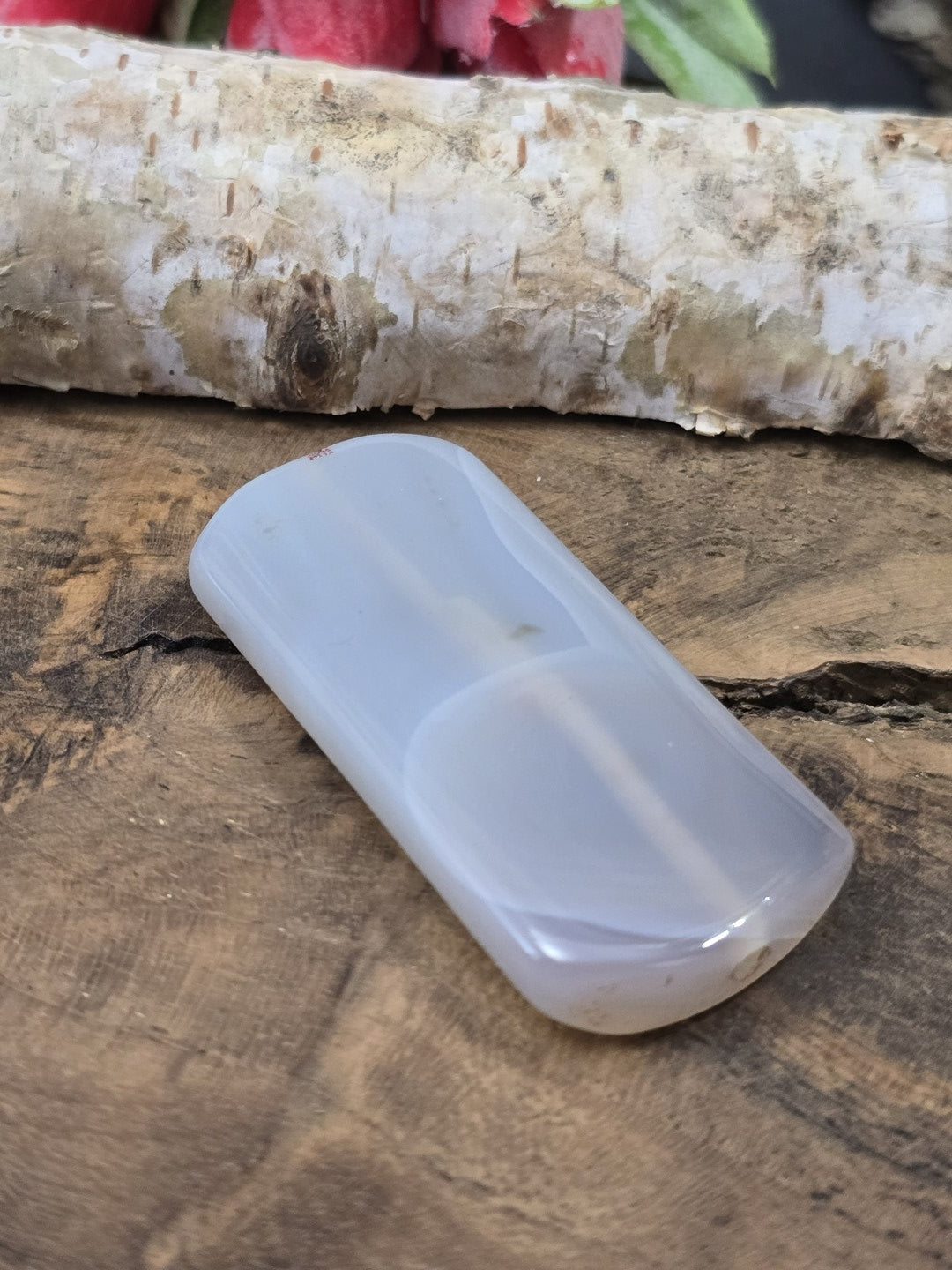 Seitliche Perspektive der flach liegenden semitransparenten Achat-Pillowperle mit sichtbarem Loch-Eingang der Fädelbohrung.