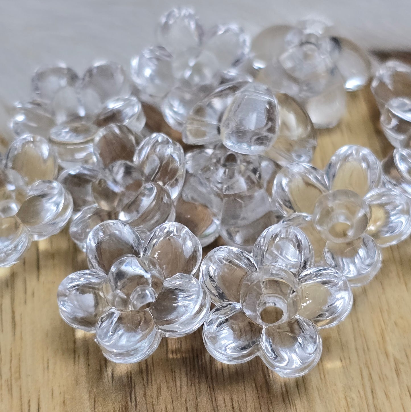 Klar transparente Acryl-Blumenperlen (18 mm) mit glänzender Oberfläche. Die filigrane Blütenform verleiht Schmuckstücken und Dekorationen eine elegante Note. Mit einem 3,5 mm großen Fädelloch lassen sie sich leicht auf Bänder oder Schnüre auffädeln. Ideal für DIY-Projekte, Hochzeiten oder Bastelarbeiten.