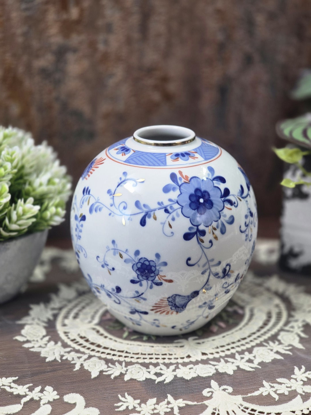 Vintage Porzellanvase in Kugelform mit kobaltblauen Blüten, feinen Ranken und Goldakzenten, frontal auf einer Spitzendecke fotografiert