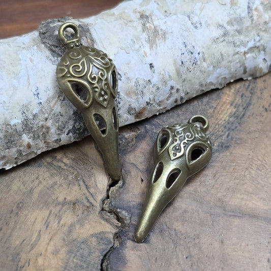 Das Bild zeigt einen detaillierten Krähenschädel mit Intarsien, gehalten in antik bronzefarbenem Finish. Er ist einseitig geprägt und hat eine hohle Rückseite, was ihn leicht und vielseitig macht.