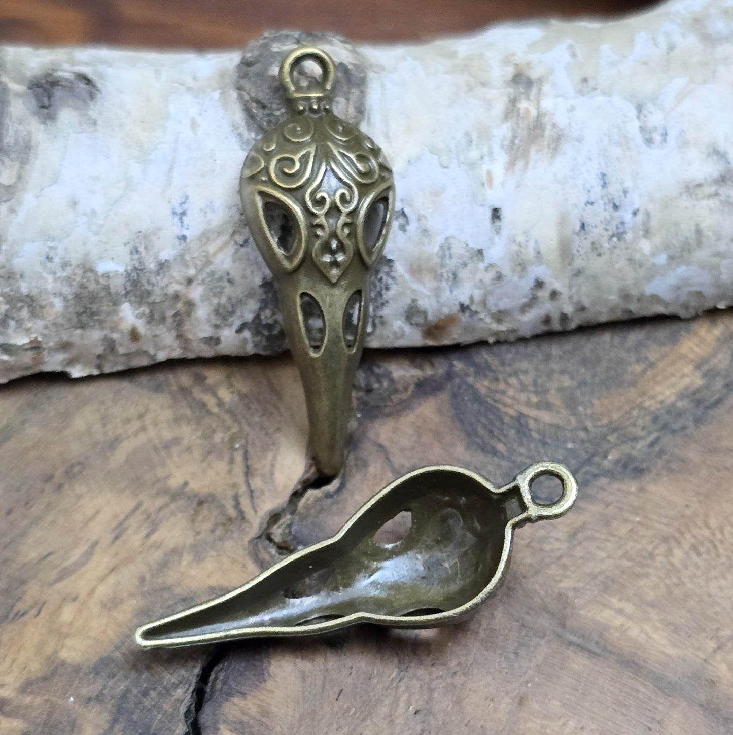Das Bild zeigt einen detaillierten Krähenschädel mit Intarsien, gehalten in antik bronzefarbenem Finish. Er ist einseitig geprägt und hat eine hohle Rückseite, was ihn leicht und vielseitig macht.