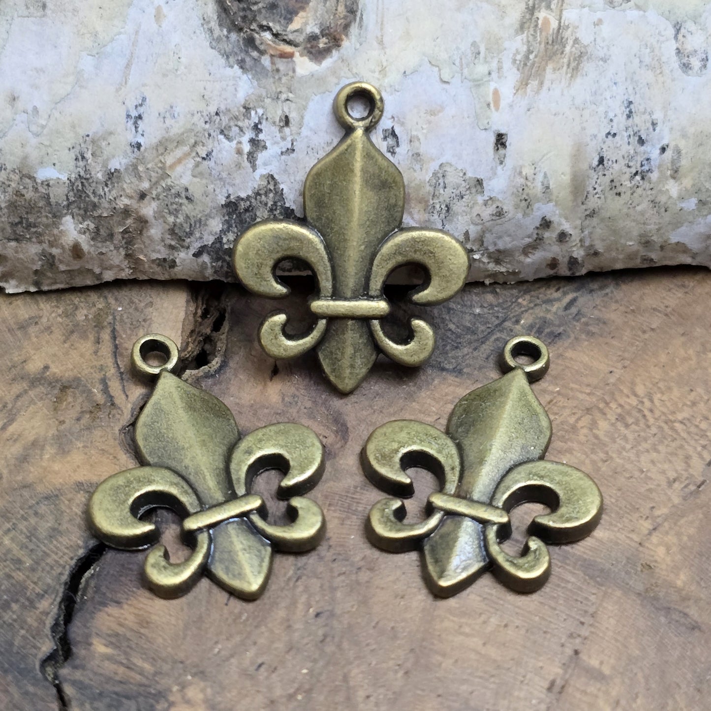 Das Bild zeigt 3 Anhänger Fleur de Lys 22mm, antik bronzefarbig. Ideal für die individuelle Schmuckfertigung.