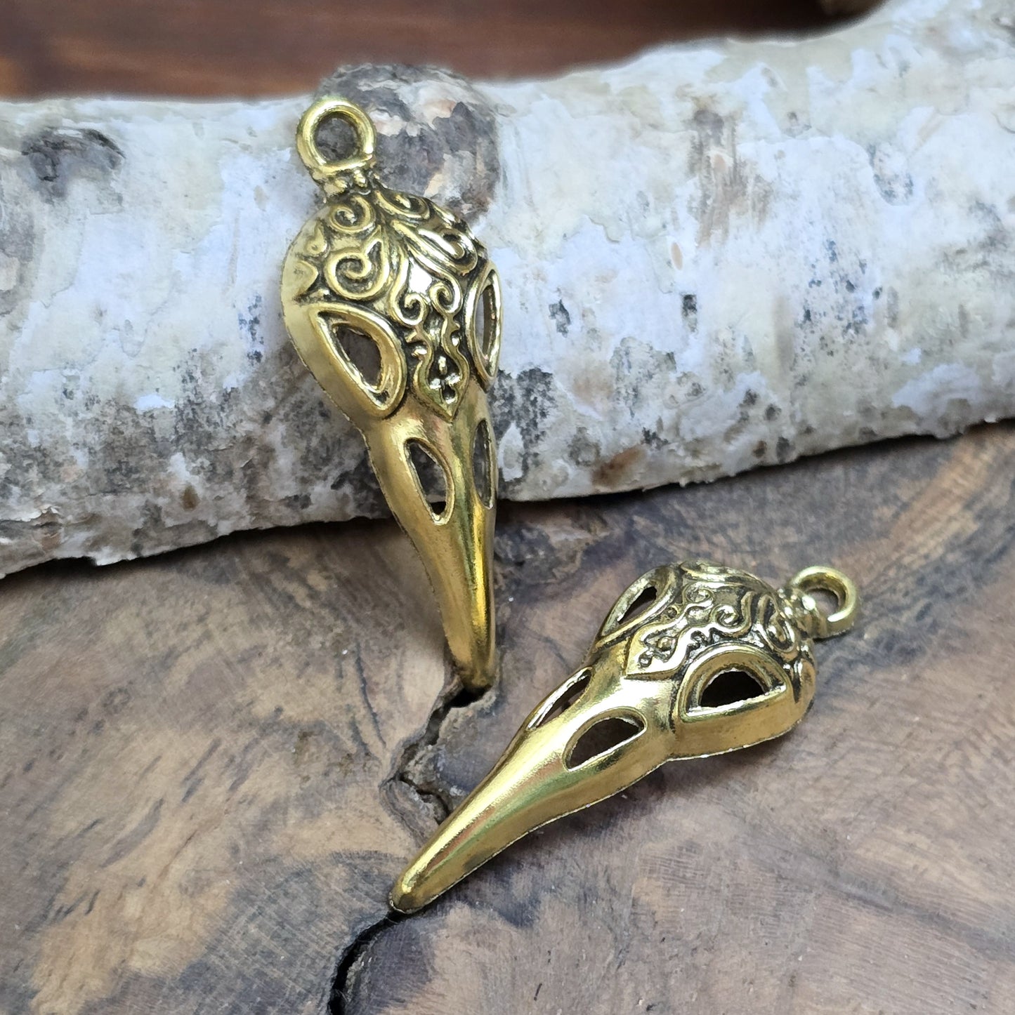 Das Bild zeigt einen detaillierten Krähenschädel mit Intarsien, gehalten in antik goldfarbenem Finish. Er ist einseitig geprägt und hat eine hohle Rückseite, was ihn leicht und vielseitig macht.