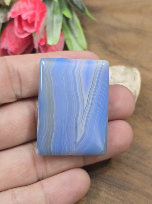 Polierter blauer Achat-Pendant in Rechteckform auf der flachen Hand als Größenvergleich für DIY-Schmuck.