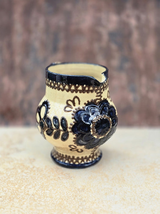 Vintage Keramikkrug im Bunzlau Stil mit cremefarbener Glasur, dunklem floralem Dekor, bauchiger Form, kleinem Ausguss und geschwungenem Henkel.