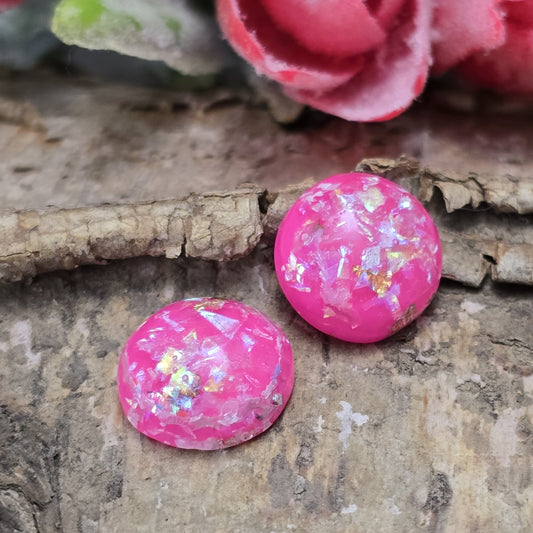 Das Bild zeigt runde Cabochons mit einem Durchmesser von 12 mm. Sie sind in einem kräftigen Pinkton gehalten und haben eine glatte, glänzende Oberfläche. Im Inneren befinden sich schimmernde Flakes, die das Licht reflektieren und für funkelnde Akzente sorgen. Je nach Lichteinfall changieren die Flakes und verleihen den Cabochons eine edle, lebendige Optik. Sie eignen sich perfekt für die Schmuckherstellung, beispielsweise für Ringe, Anhänger oder Ohrstecker.
