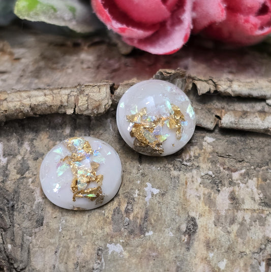 Das Bild zeigt runde Cabochons mit einem Durchmesser von 12 mm. Sie sind milchig-weiß und haben eine glatte, glänzende Oberfläche. Im Inneren der Cabochons sind feine, schimmernde Flakes eingearbeitet, die je nach Lichteinfall dezent funkeln. Die Flakes reflektieren das Licht in sanften, leicht changierenden Tönen. Die Cabochons wirken edel und leicht transparent. Sie eignen sich für die Schmuckherstellung, beispielsweise für Ringe, Anhänger oder Ohrstecker.