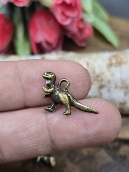 Ein kleiner antik-bronze T-Rex Dino-Anhänger auf einer Fingerkuppe präsentiert als praktischer Größenvergleich für DIY-Schmuckprojekte.