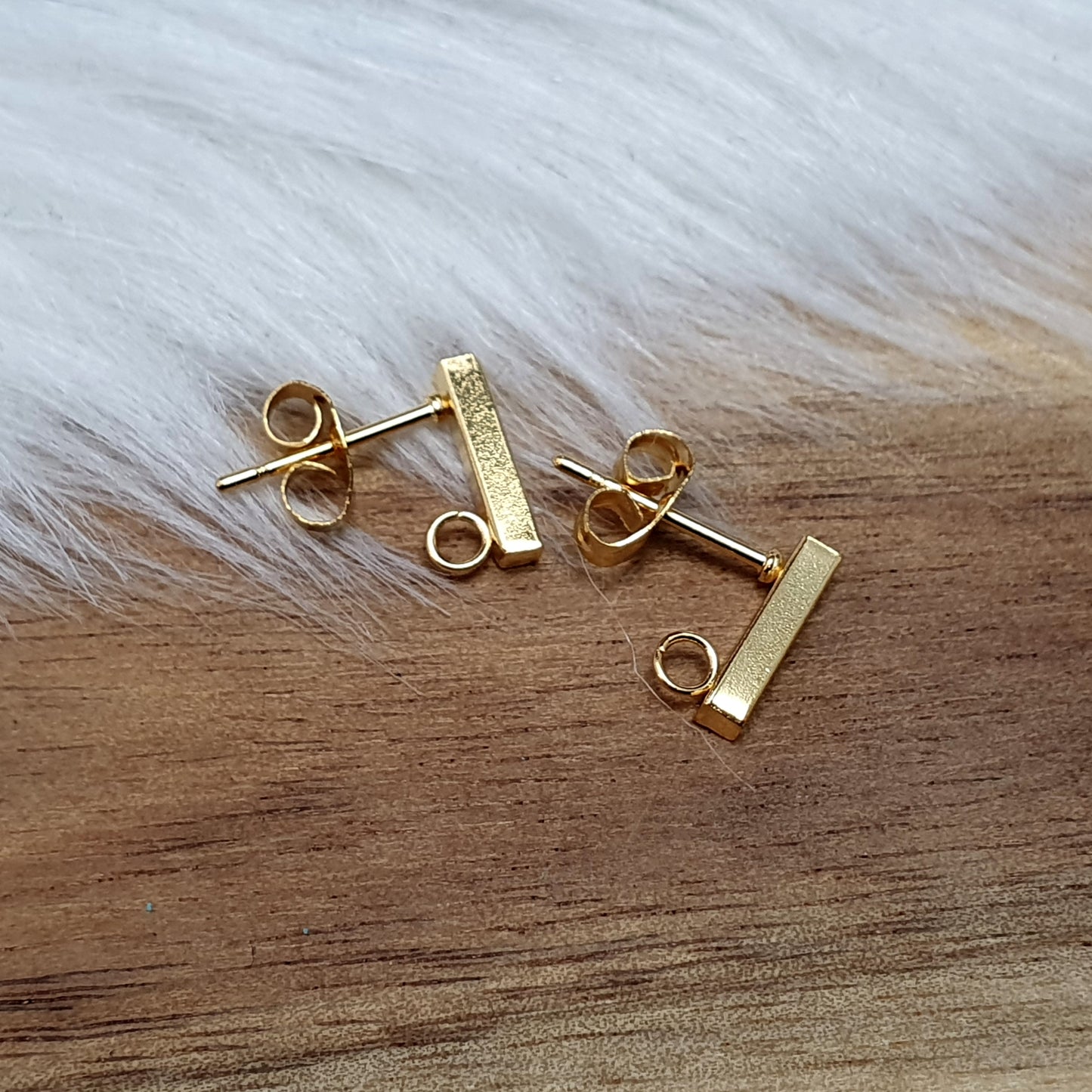 Das Bild zeigt goldfarbige Ohrstecker aus Edelstahl in Stäbchenform mit Öse & Flügelmuttern.