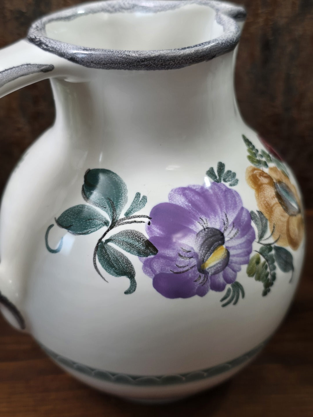 Vintage Keramikkrug mit violetter Blüte, grünen Blättern und ockerfarbenem Blütenmotiv unter dem grau geränderten Ausguss.