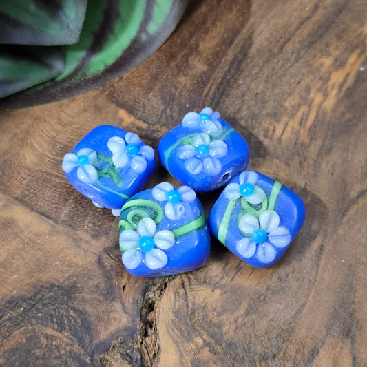 4 handgefertigte Lampwork-Glasperlen, quadratisch in Blau mit Blütendekor. Hochwertiges Material für individuelle Schmuckherstellung.