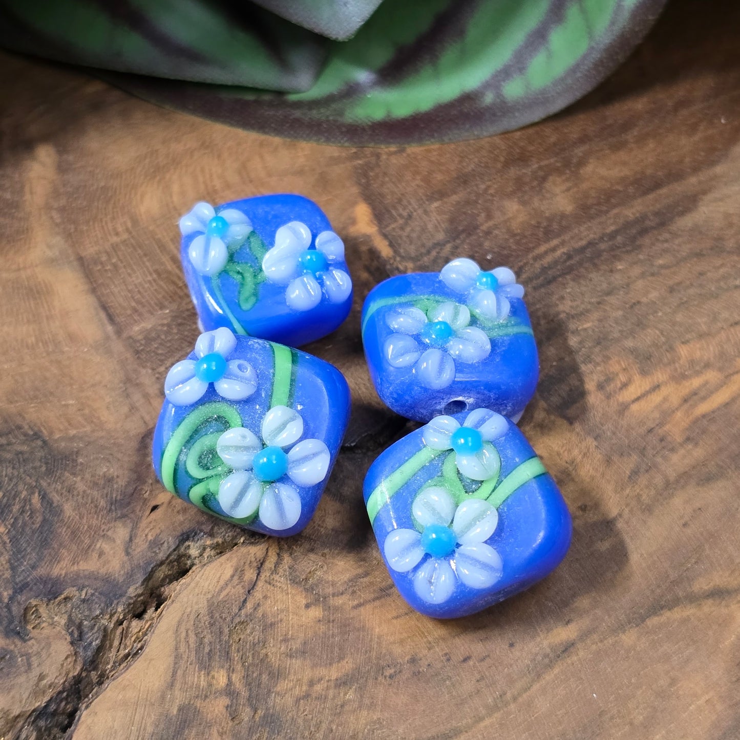 4 handgefertigte Lampwork-Glasperlen, quadratisch in Blau mit Blütendekor. Hochwertiges Material für individuelle Schmuckherstellung.