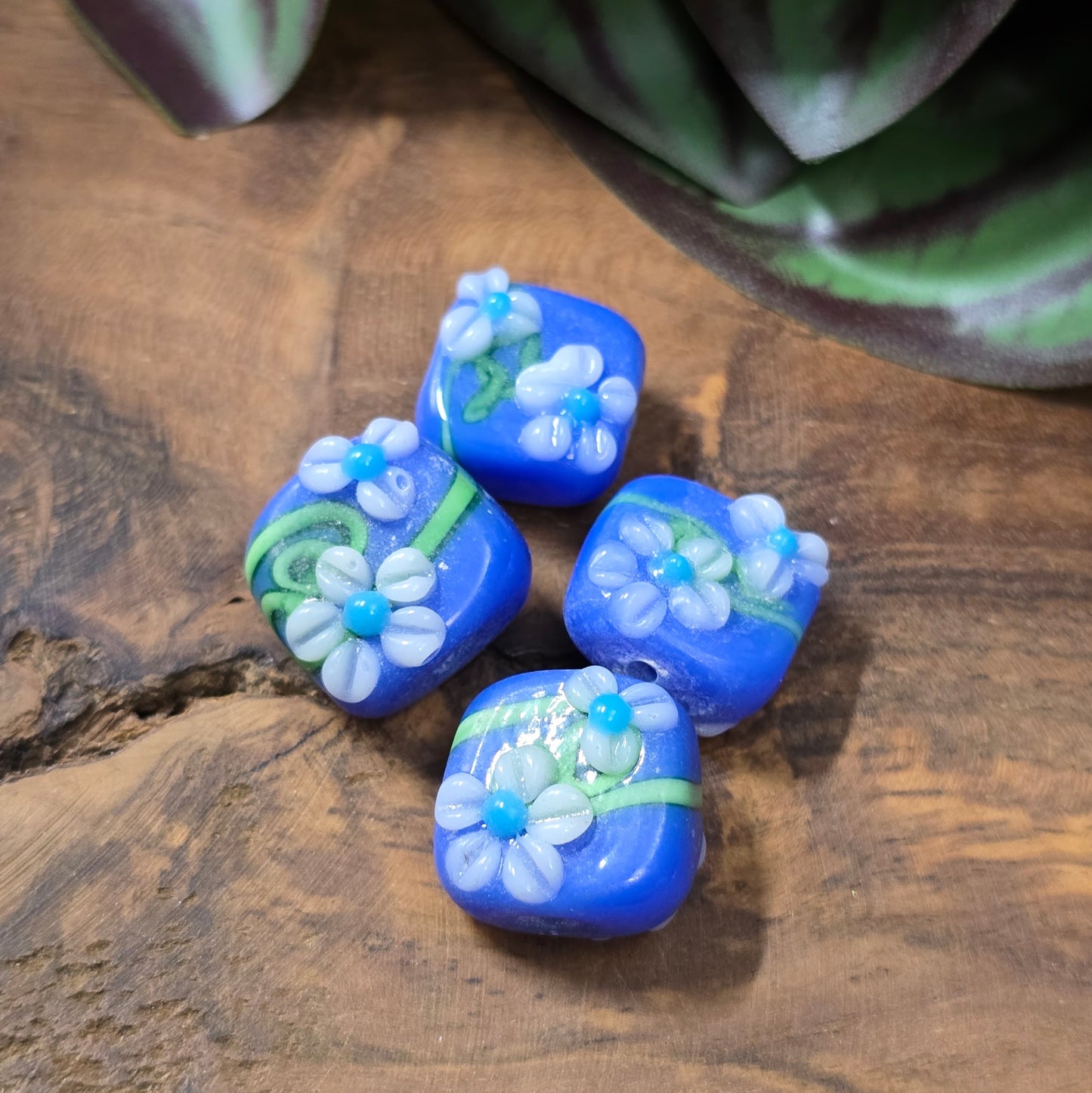 4 handgefertigte Lampwork-Glasperlen, quadratisch in Blau mit Blütendekor. Hochwertiges Material für individuelle Schmuckherstellung.