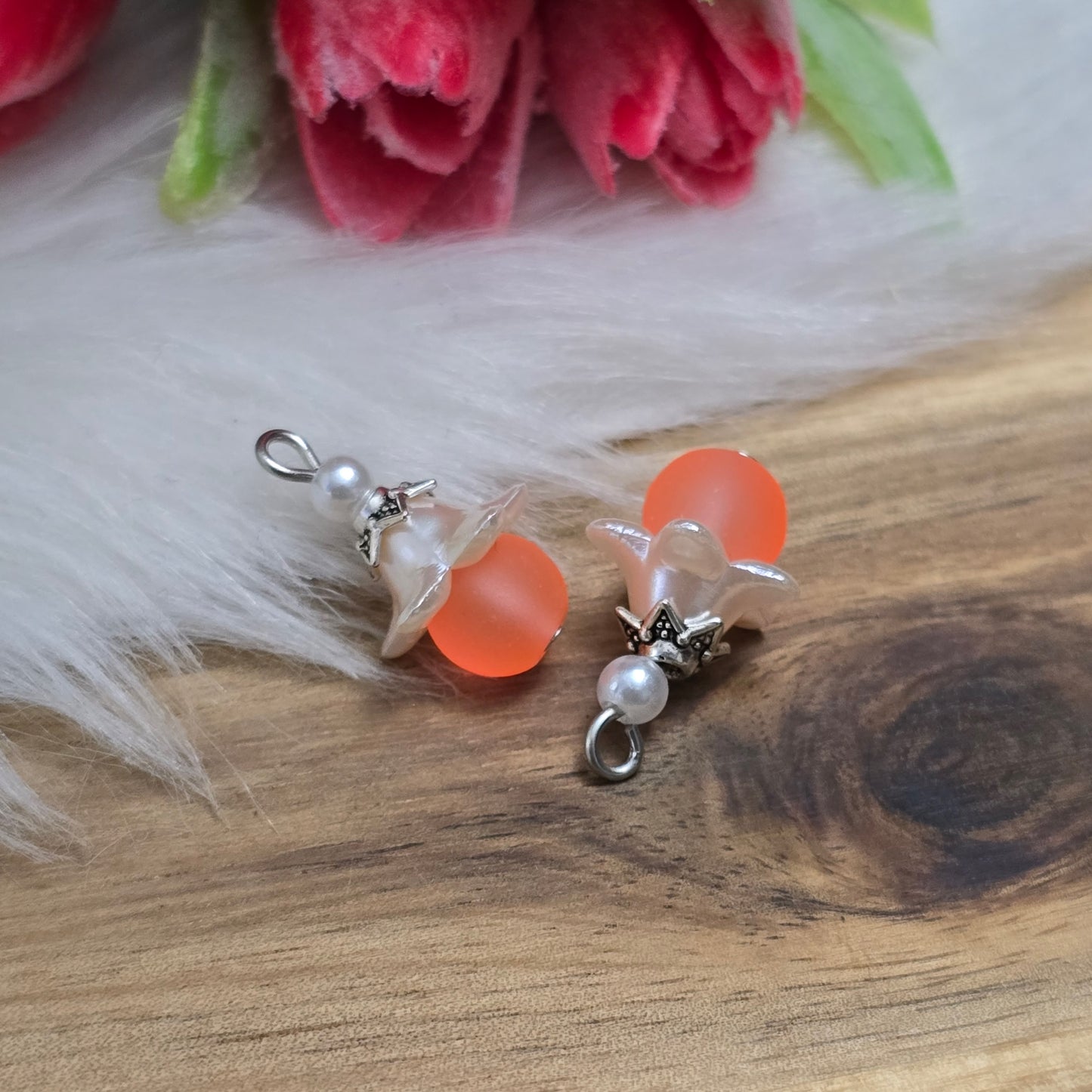 Das Bild zeigt zwei handgemachte Anhänger mit matten, orangefarbenen Glasperlen. Jedes Stück verfügt über ein elegantes, weißes Acrylblütenkäppchen, das einen verspielten Akzent setzt. Die antik silberfarbigen Perlenkappen runden das Design harmonisch ab. Mit einem Durchmesser von etwa 20mm sind die Anhänger filigran und ideal für Schmuckprojekte. Die Kombination aus lebendigen Farben und stilvollen Materialien verleiht den Anhängern einen attraktiven Look, der in jeder Schmuckkollektion hervorsticht.