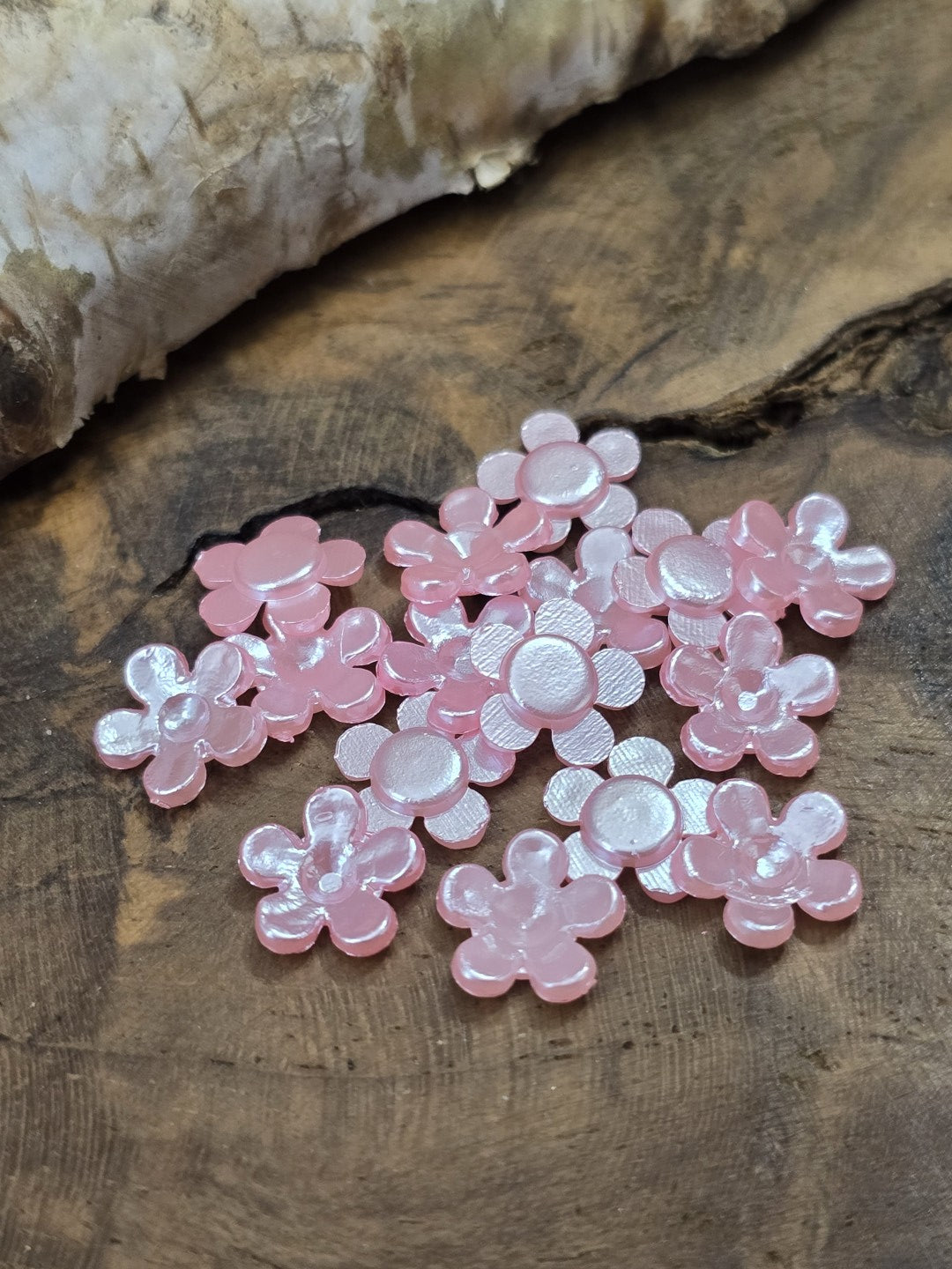 Mehrere 8 mm Cabochon-Blüten in Rosa zum Aufkleben, teils mit der flachen Unterseite nach oben zeigend zur Ansicht der Klebefläche.