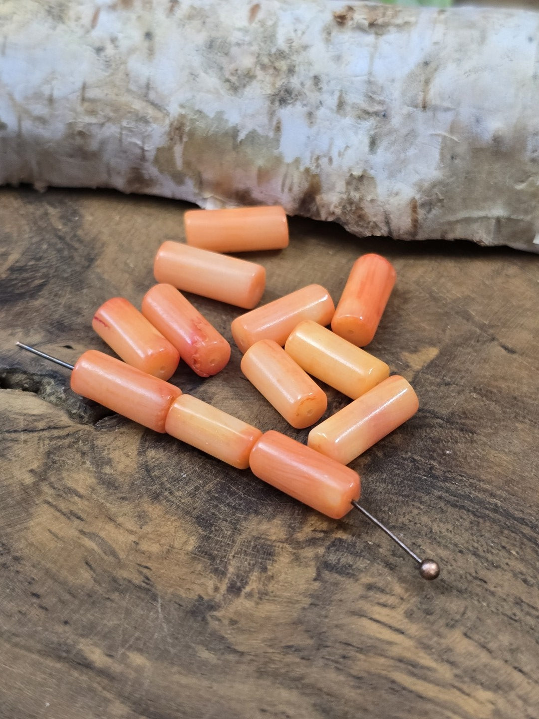 Perspektivische Ansicht von aufgereihten lachs-orangefarbenen Walzenperlen aus Koralle neben weiteren losen Perlen.