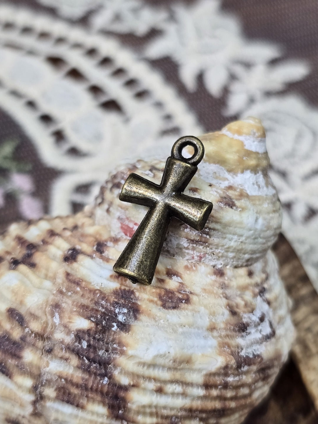 Schlichter Vintage-Kreuz-Schmuckanhänger aus Metall aufgestellt vor einer dekorativen Muschel.