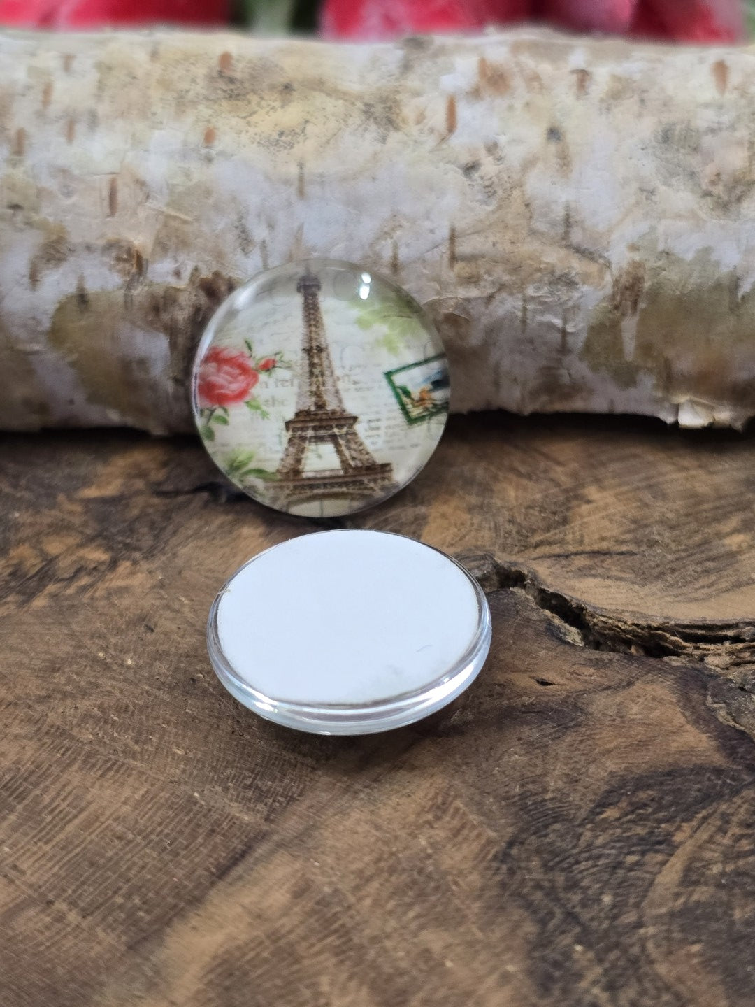 Zwei runde 16 mm Paris-Glascabochons auf Holz, wobei einer flach auf der weißen Rückseite liegt, um die Klebefläche für Fassungen zu zeigen.