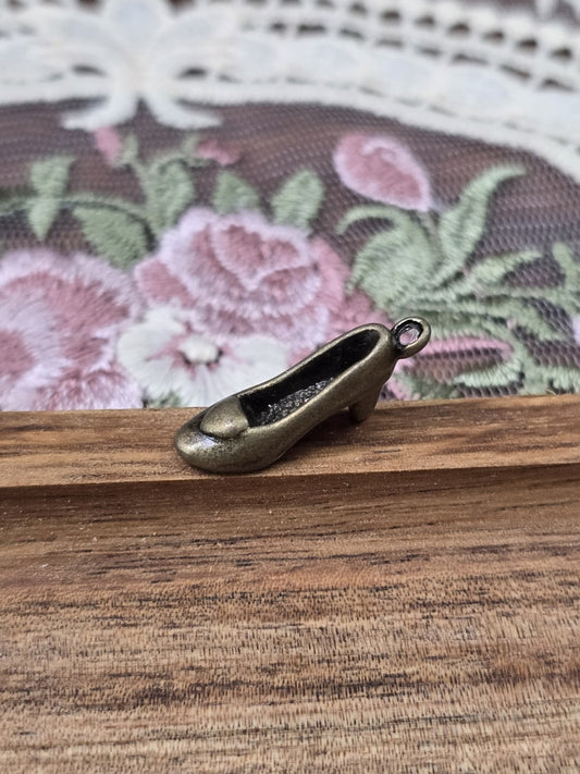 Dreidimensionaler Pumps-Anhänger in Bronze-Optik seitlich auf Holz platziert.
