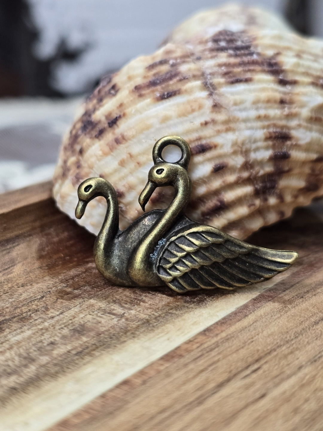 Schwanen-Schmuckanhänger in Bronze-Optik mit Öse stehend vor einer Dekomuschel.