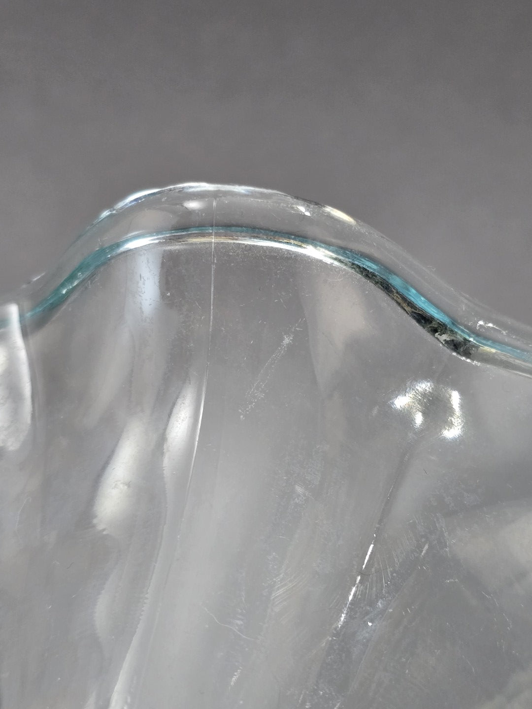 Nahaufnahme des gewellten Glasrands mit hellblauer Tönung, glänzender Oberfläche und kleinen sichtbaren Spuren im transparenten Glas.
