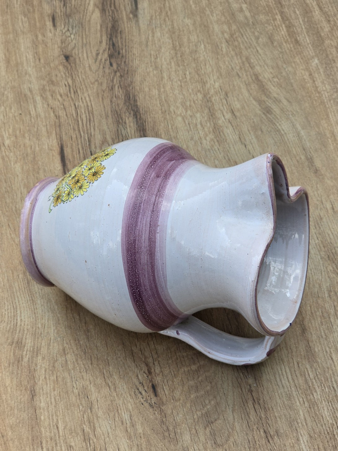 Liegender Vintage Studiokeramik Krug mit Henkel, violettem Streifendekor und gelbem Blumendetail auf Holzfläche.