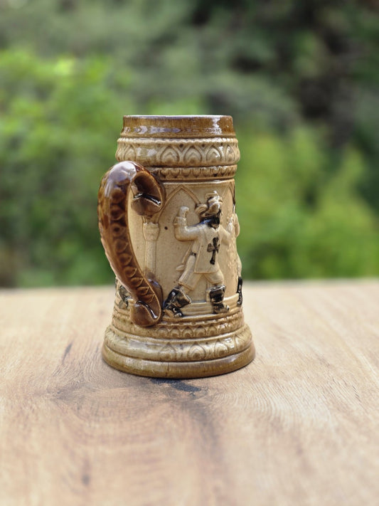 Braun-beiges Westerwald Bierseidel mit Landsknecht Relief, Tatzenkreuz auf der Brust, geschwungenem Henkel und kleiner Chipstelle am Standring.