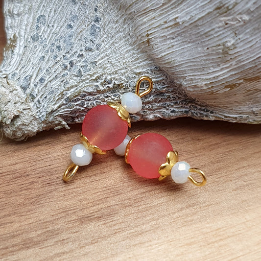 Die handgefertigten Schmuckverbinder bestehen aus mattierten lachsfarbenen Glasperlen, die von vergoldeten Metallelementen umrahmt werden. Ihre warme Farbgebung und die weiche Oberfläche verleihen ihnen eine elegante, dezente Ausstrahlung. Mit einer Länge von 24 mm sind sie perfekt als stilvolle Verbindungselemente oder als dezenter Blickfang in Schmuckstücken. Dank der beidseitigen Ösen lassen sie sich vielseitig für Ketten, Armbänder oder Ohrringe verwenden.