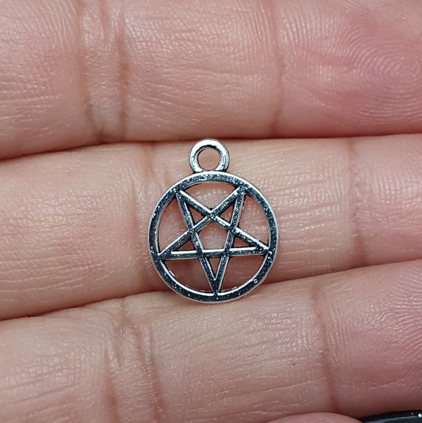 Auf dem Bild sind kleine Anhänger abgebildet, die die Form eines invertierten Pentagramms haben und in antik silberner Farbe gehalten sind. Jeder dieser Anhänger ist in einem Ring eingefasst und misst ungefähr 16 x 13 mm. Die Oberfläche der Anhänger weist eine feine Struktur auf und besitzt eine metallische Beschaffenheit, die das Licht reflektiert und ihnen einen attraktiven Glanz verleiht.