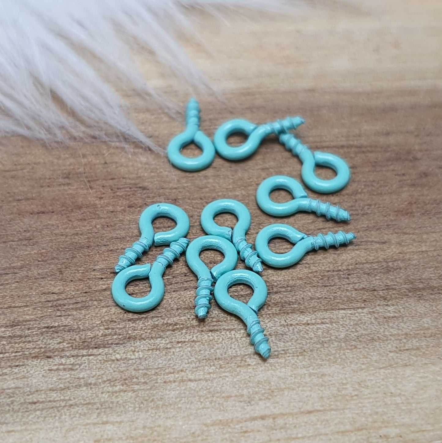 Das Bild zeigt ein Set von 10 farbig lackierten Schraubösen in verschiedenen lebhaften Farben, darunter Hellblau, Grün, Rot, Aqua, Weiß und Rosa. Jede Schrauböse hat die Abmessungen von ca. 8x4mm und ist sorgfältig gestaltet, um eine einfache Anwendung zu ermöglichen. Die Schraubösen sind ideal für das Einschrauben in Materialien wie Holz, Resin oder Acryl, um individuelle Anhänger zu kreieren. Die glänzende Oberfläche der Schraubösen sorgt für einen attraktiven Look, der jedem kreativen Projekt einen farbe