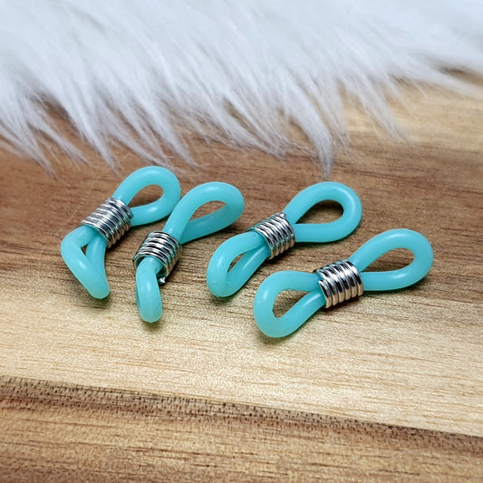 Das Bild zeigt eine Auswahl an Silikonschlaufen für Brillenketten und Maskenhalter in drei Farben: Mint, Rosa und Schwarz. Jede Schlaufe hat eine flexible, weiche Textur und ist so gestaltet, dass sie einfach auf den Bügel der Brille geschoben werden kann. An einem Ende der Schlaufe befindet sich ein kleiner Metallring, der fest angebracht ist, um ein Abrutschen zu verhindern. Die anderen Enden der Schlaufen sind offen, sodass sie mit einem Karabiner oder Biegering leicht an einer Kette befestigt werden kön