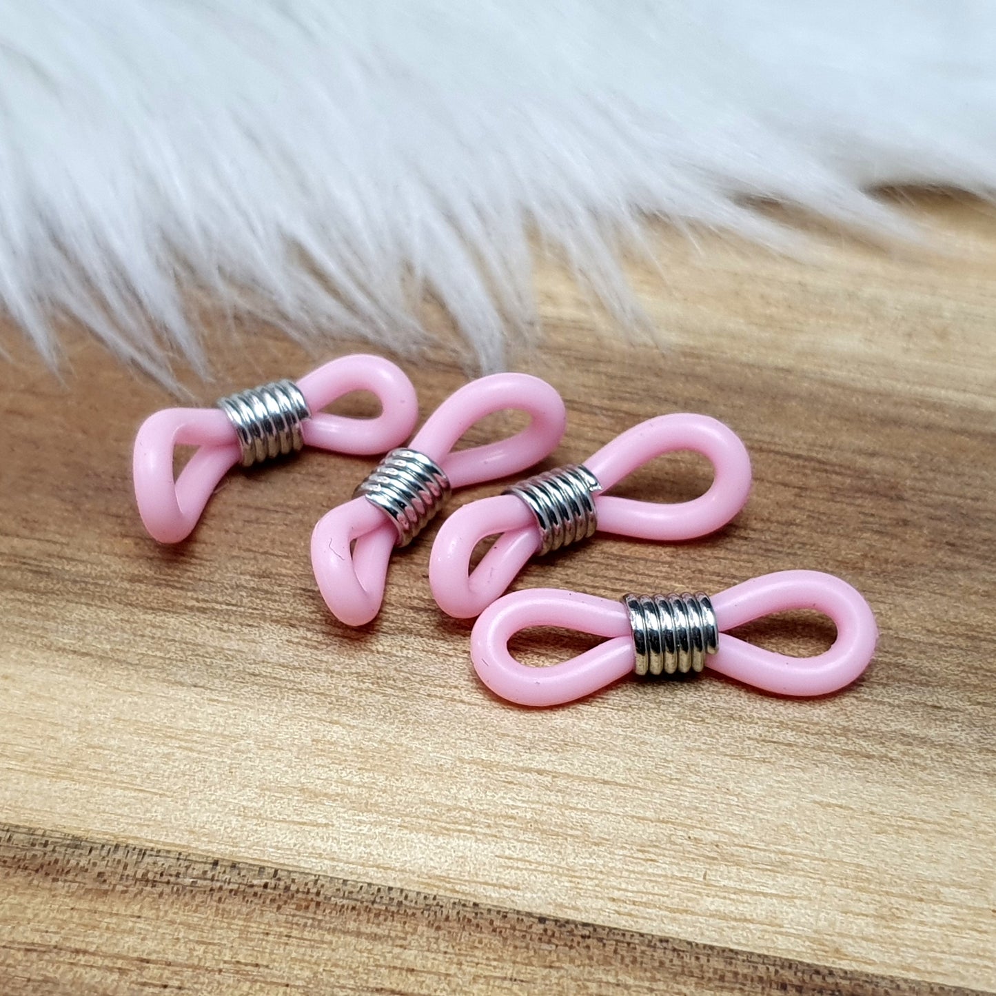 Das Bild zeigt eine Auswahl an Silikonschlaufen für Brillenketten und Maskenhalter in drei Farben: Mint, Rosa und Schwarz. Jede Schlaufe hat eine flexible, weiche Textur und ist so gestaltet, dass sie einfach auf den Bügel der Brille geschoben werden kann. An einem Ende der Schlaufe befindet sich ein kleiner Metallring, der fest angebracht ist, um ein Abrutschen zu verhindern. Die anderen Enden der Schlaufen sind offen, sodass sie mit einem Karabiner oder Biegering leicht an einer Kette befestigt werden kön