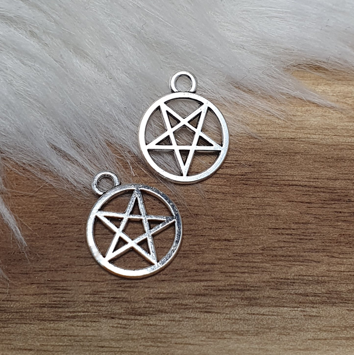 Auf dem Bild sind kleine Anhänger abgebildet, die die Form eines invertierten Pentagramms haben und in antik silberner Farbe gehalten sind. Jeder dieser Anhänger ist in einem Ring eingefasst und misst ungefähr 16 x 13 mm. Die Oberfläche der Anhänger weist eine feine Struktur auf und besitzt eine metallische Beschaffenheit, die das Licht reflektiert und ihnen einen attraktiven Glanz verleiht.