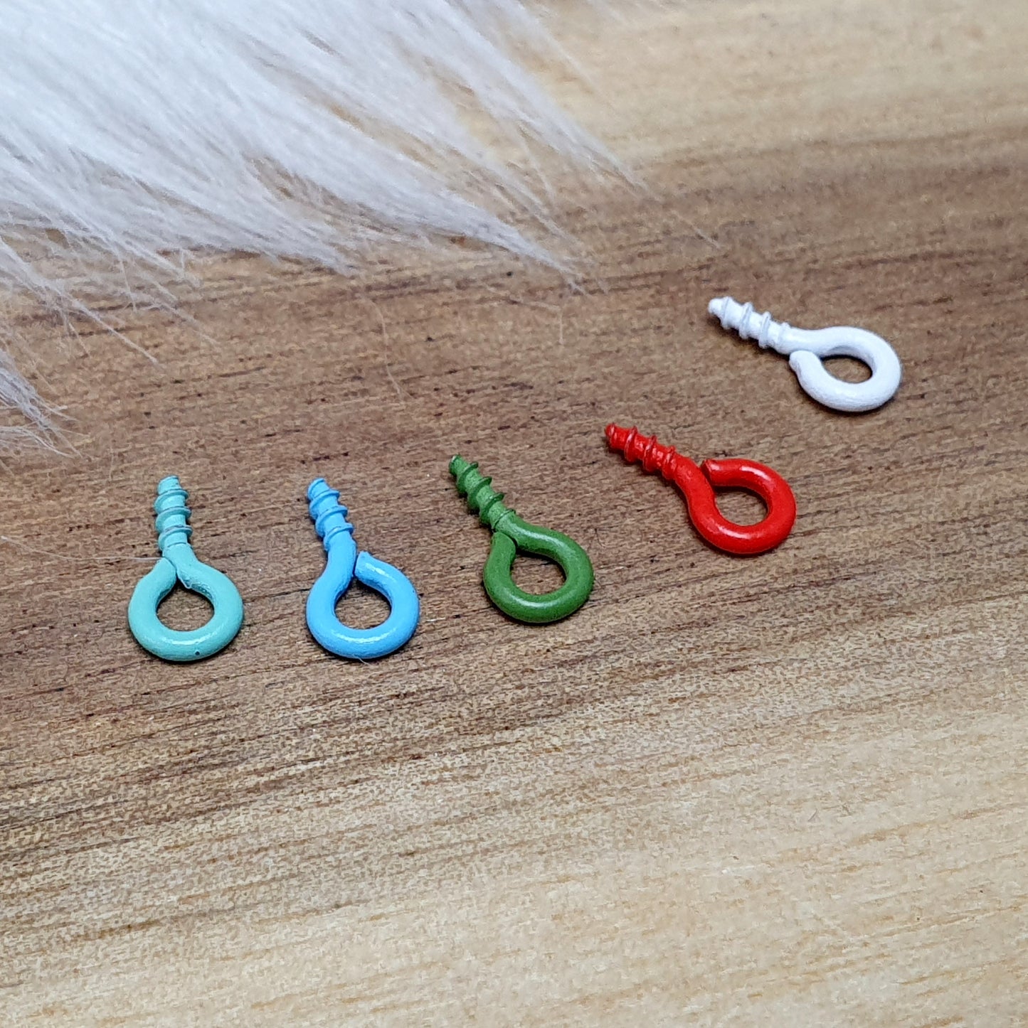Das Bild zeigt ein Set von 10 farbig lackierten Schraubösen in verschiedenen lebhaften Farben, darunter Hellblau, Grün, Rot, Aqua, Weiß und Rosa. Jede Schrauböse hat die Abmessungen von ca. 8x4mm und ist sorgfältig gestaltet, um eine einfache Anwendung zu ermöglichen. Die Schraubösen sind ideal für das Einschrauben in Materialien wie Holz, Resin oder Acryl, um individuelle Anhänger zu kreieren. Die glänzende Oberfläche der Schraubösen sorgt für einen attraktiven Look, der jedem kreativen Projekt einen farbe
