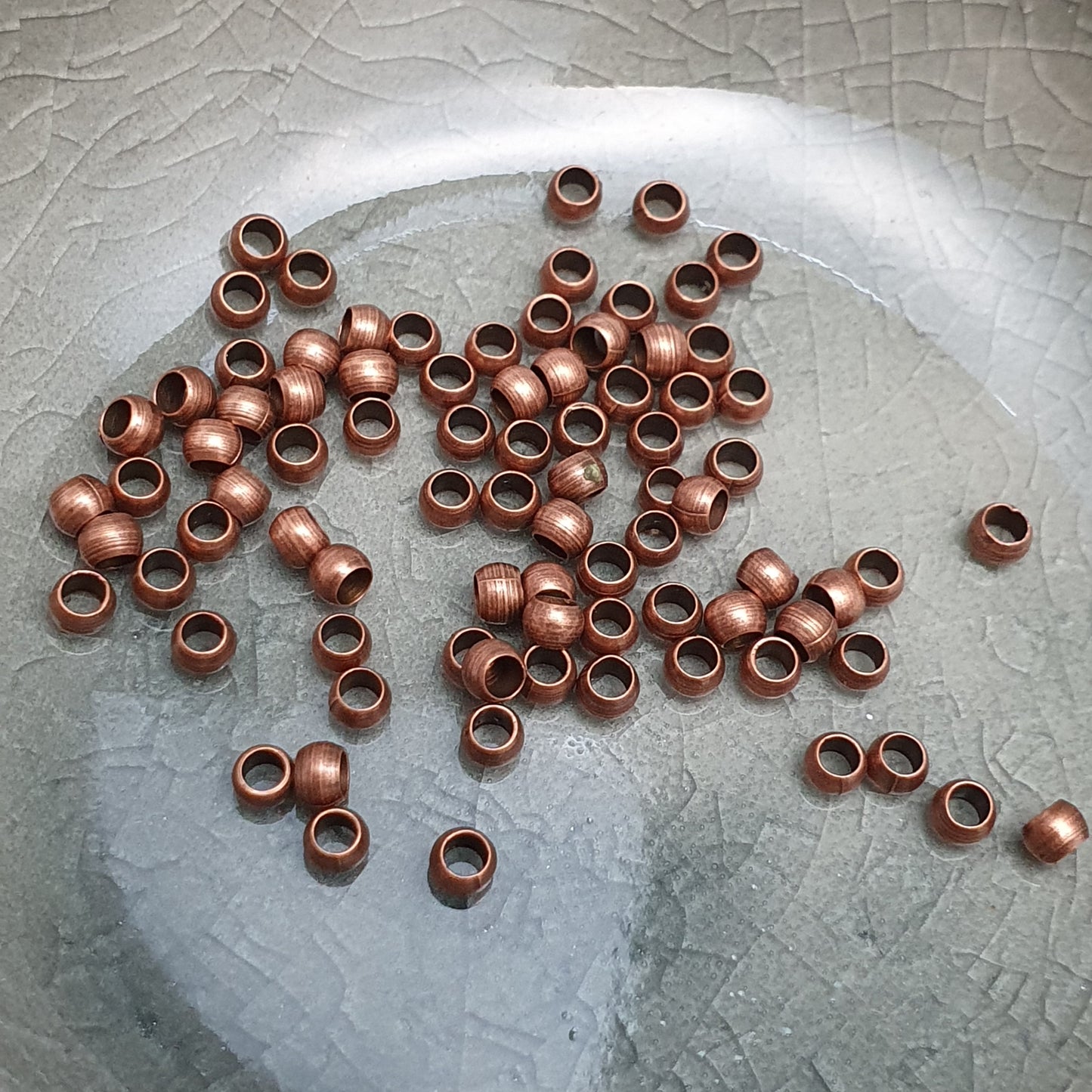 Das Bild zeigt Quetschperlen in Kugelform, antik kupferfarbig mit einem Durchmesser von 2,5mm. Ideal zum Fixieren von Perlen.