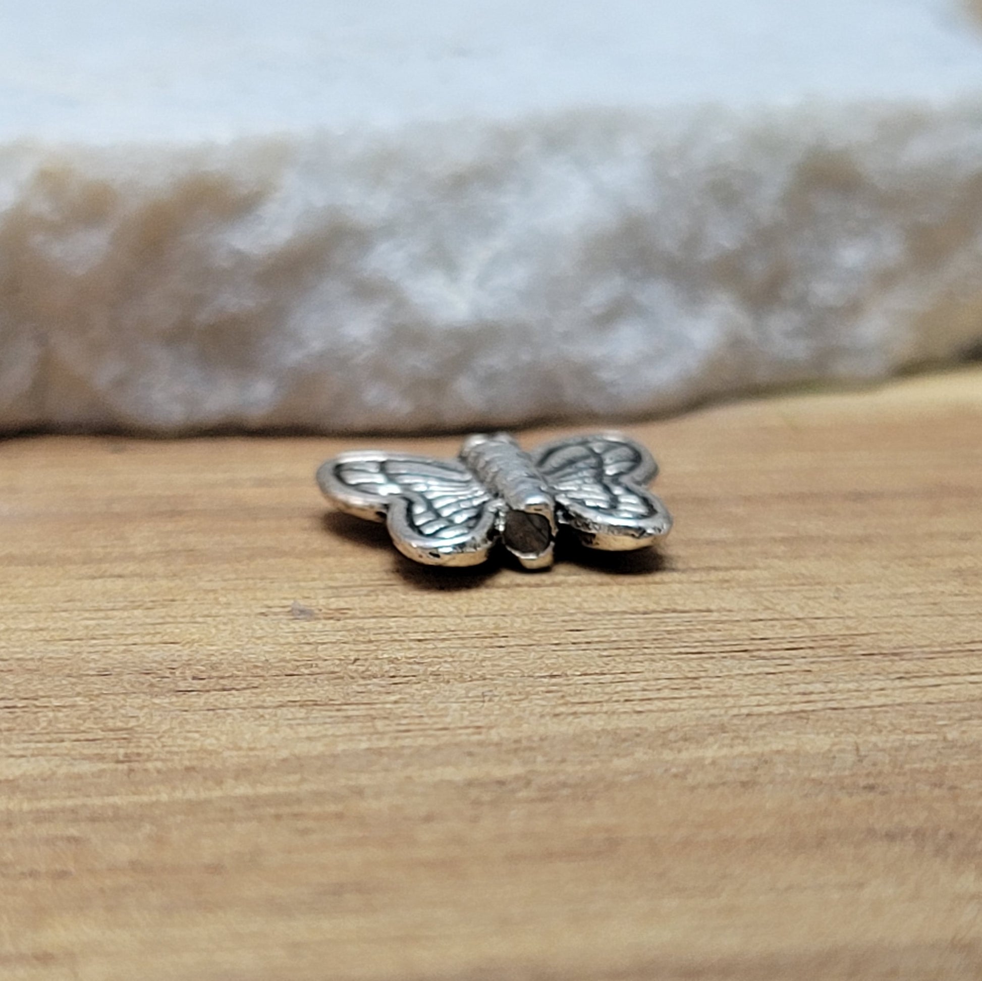 Eine Packung mit 5 Metallperlen in Form eines Schmetterlings.  Die Perlen sind beidseitig geprägt, antik silberfarbig und haben eine hübsches Antikfinish, was für einen tollen Vintage-Effekt sorgt.  Das Fädelloch verläuft von oben nach unten durch den Schmetterling. 