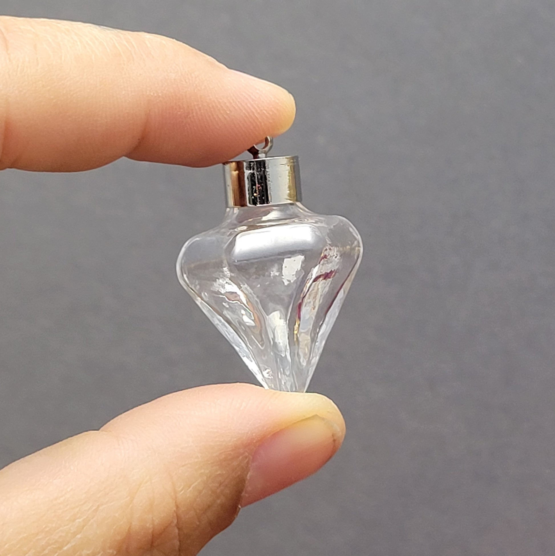 Anhänger Glasflasche in konischer Form, ideal zum befüllen.  Die Glasflasche hat eine nach unten spitz zulaufende Form mit sechs flachen Seiten und einer Öffnung oben. Diese Öffnung bietet Platz für eine Vielzahl von Materialien, darunter Edelsteinsplitter, Sand, Glitzer, Granulat und sogar Flüssigkeiten (bitte beachten Sie die Öffnungsgröße).