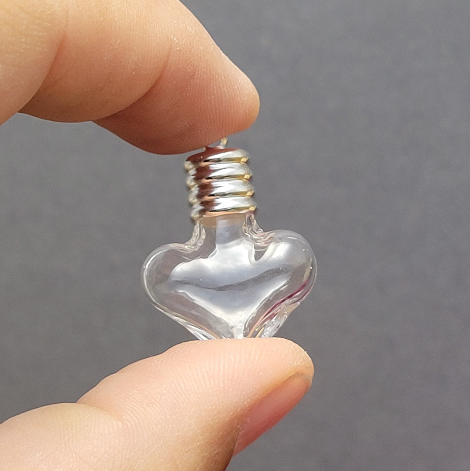 Anhänger kleine Glasflasche in Form eines Herzens zum befüllen.  Die Glasflasche hat oben eine Öffnung oben und bietet Platz für eine Vielzahl von Materialien, darunter (wirklich kleine) Edelsteinsplitter, Sand, Glitzer, und Granulat (bitte beachten Sie die Öffnungsgröße). 