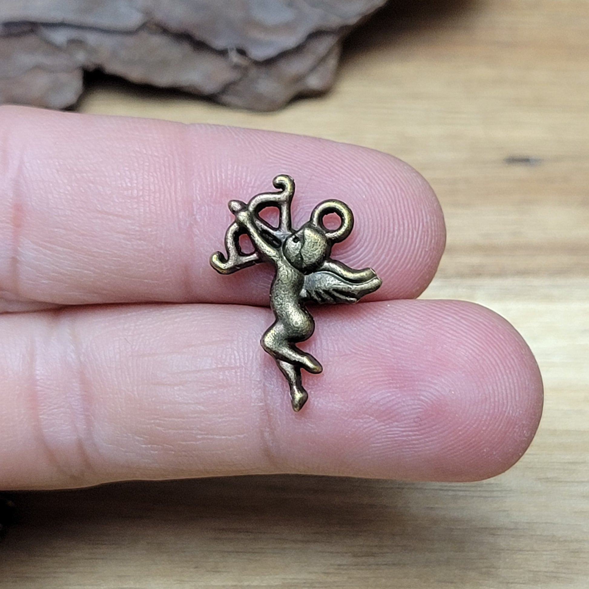 ein kleiner Charms Armor in antik bronzefarbig liegend auf zwei Fingern zur Größenreferenz