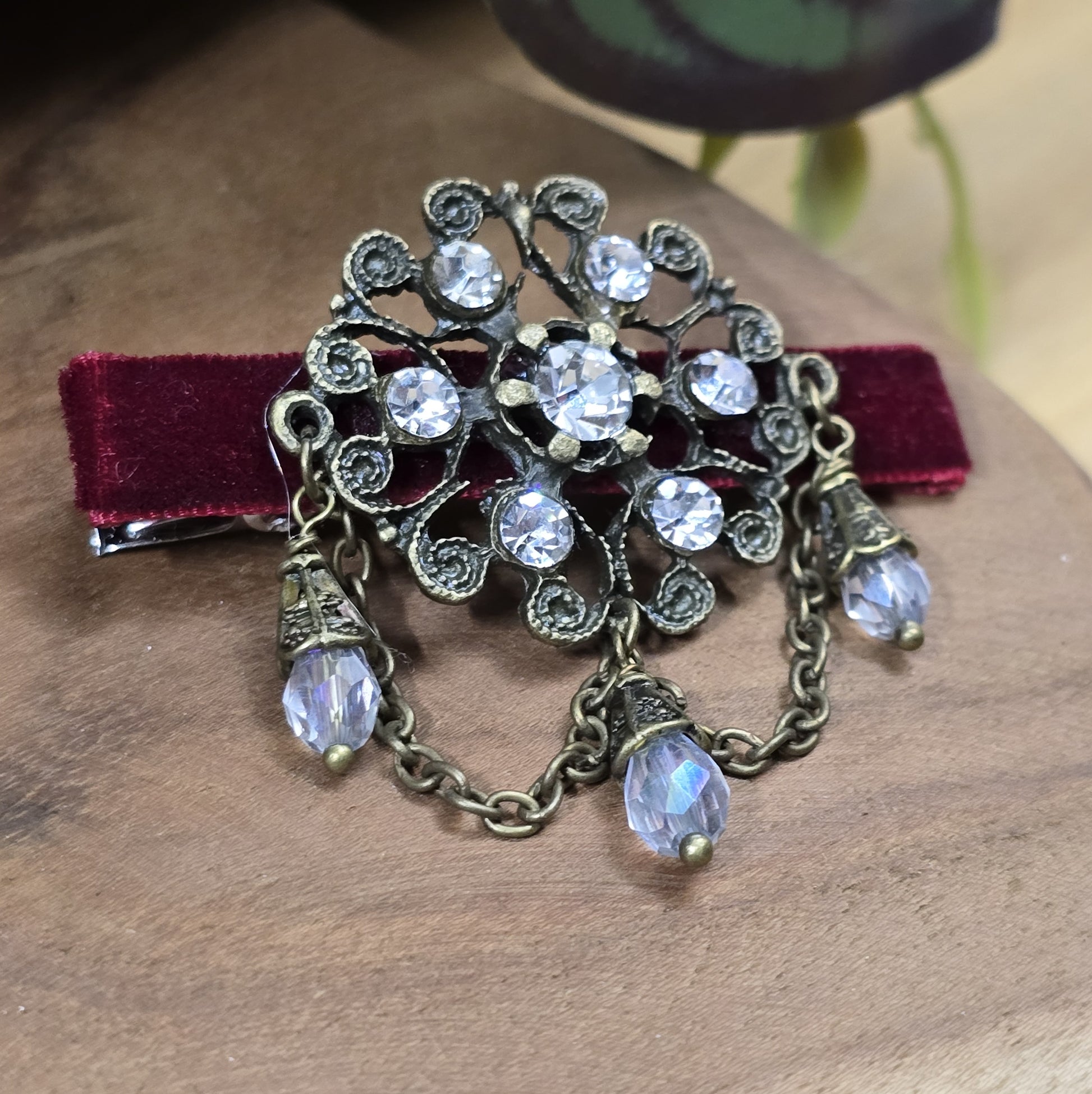Das Bild zeigt eine Krokodilspange im Vintagelook mit Strass und dunkelrotem Samt, Kristallglasanhänger, Kettchen, Einzelstück

Lass dich von der zeitlosen Eleganz vergangener Epochen verzaubern mit dieser exquisiten Krokodilspange im Vintagestil. Sie ist kunstvoll verziert mit einem filigranen, antik bronzefarbigen Schmuckteil, welches mit funkelndem Strass besetzt ist. 